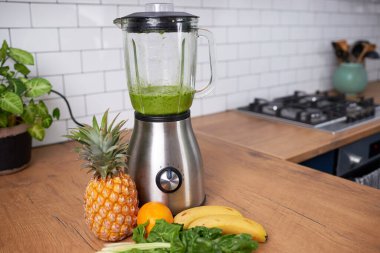 Still life of a blender with fresh green smoothie and fruit on display in kitchen. High quality photo