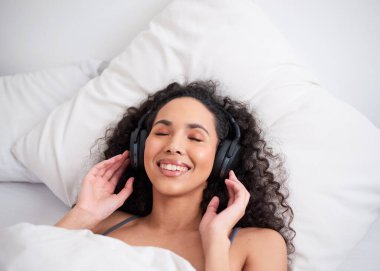 Yatakta kulaklıkla yatan çok ırklı genç bir kadının yukarıdan çekilmiş fotoğrafı. Yüksek kalite fotoğraf