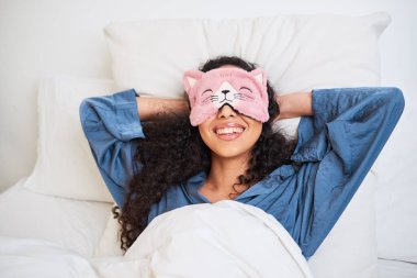 Çok ırklı genç bir kadın, sevimli bir kedi yavrusu uyku maskesiyle yatakta uyanıyor. Yüksek kalite fotoğraf