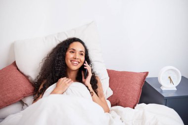 Genç, çok ırklı bir kadın, yataktan şehirlerarası samimi telefon konuşmalarında güler. Yüksek kalite fotoğraf