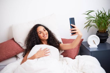 Genç bir nüfuzlu, yatakta uyanırken selfie çeker. Yüksek kalite fotoğraf