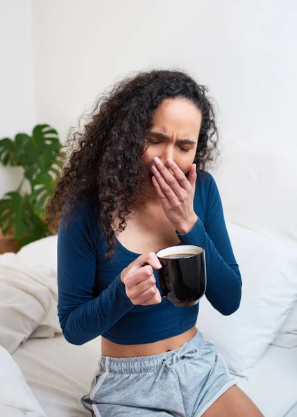 A beautiful young woman yawns and struggles to wake up in bed with mug of coffee. High quality photo