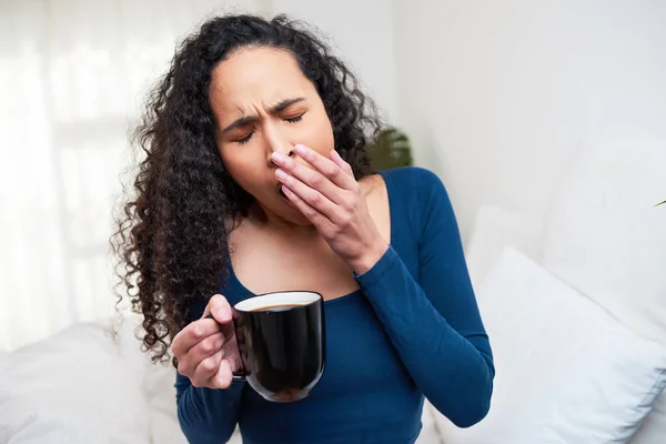 A beautiful young woman yawns and struggles to wake up in bed with mug of coffee. High quality photo