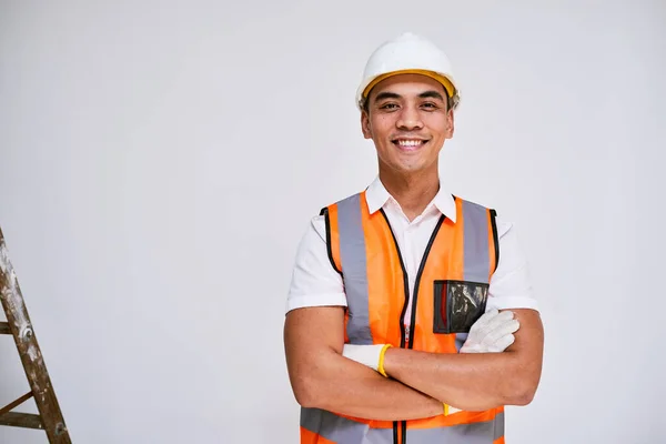 Portrait of an Asian construction worker smiling with arms crossed, white wall. High quality photo