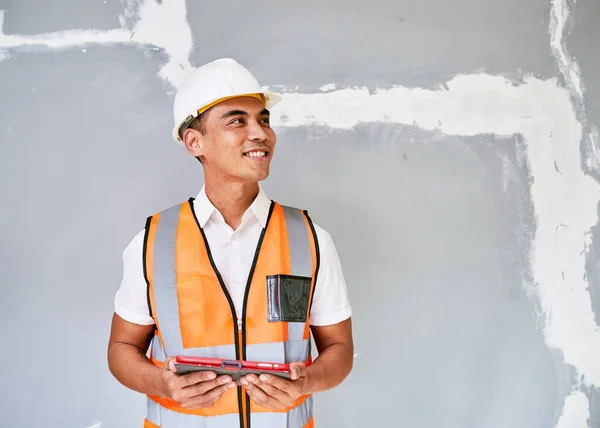 A young Asian construction worker looks to the right in front of cracked wall. High quality photo