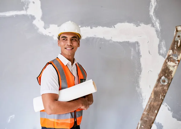An attractive Asian construction worker holds building plans under his arm. High quality photo
