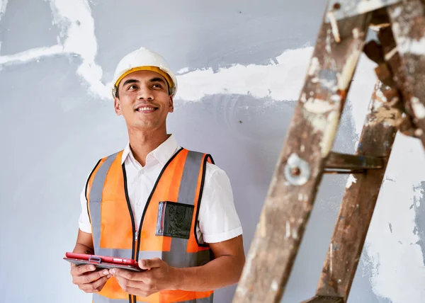 A young Asian construction worker looks to the right in front of cracked wall. High quality photo