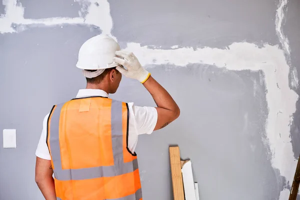 A construction worker scratches head in confusion while looking at fixed crack. High quality photo