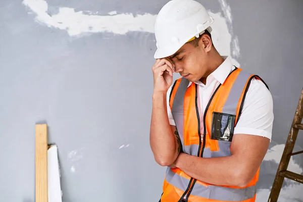 A young Asian construction worker rubs his temples in pain on site. High quality photo