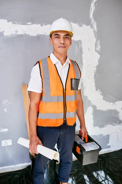 Portrait of a construction supervisor on site with building plans and toolbox. High quality photo