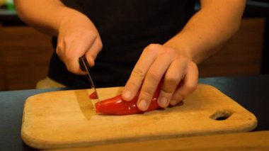 Bir adam mutfakta kırmızı biberi bıçakla kesiyor. Sıcak sarı ışık