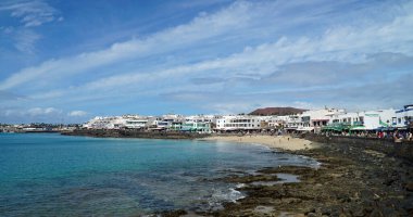 PLAYA BLANCA, LANZAROTE, SPAIN - 22 Mart 2022: Playa Blanca şehir plajı ve deniz kenarındaki dükkanlar ve restoranlar .
