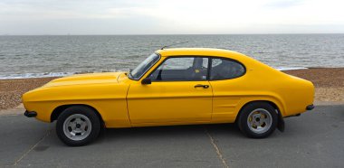 FELIXSTOWE, SUFFOLK, ENGLAND - MAY 01, 2022: Classic Yellow Ford Capri GT Parked on seafront promenade ocean in background.