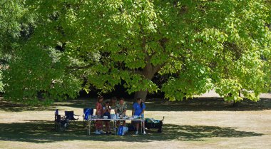 SILSOE, BEDFORDSHIRE, ENGLAND - AUGUST 10, 2022: People setting up Picnic with tables under a tree.