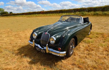 LITTLE GRANSDEN, CAMBRIDGESHIRE, ENGLAND - AUGUST 28, 2022: Classic 1960 Jaguar XK150 drop head coupe parked in field.