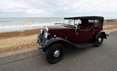 FELIXSTOWE, SUFFOLK, ENGLAND - MAYIS 05, 2022: Arka planda deniz kenarında park edilmiş klasik Red Morris 8 motorlu araba.
