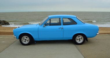 FELIXSTOWE, SUFFOLK, ENGLAND - 27 AĞUSTOS 2016: Arka planda deniz kenarında park edilmiş klasik Açık Mavi Ford Eskort Otomobili.