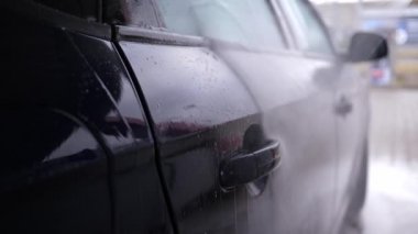 Arabanın yüzeyindeki köpüğü su püskürtücü jetle yıkıyor. Şoför arabasını tek başına yıkıyor.