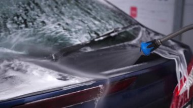 Arabanın yüzeyindeki köpüğü su püskürtücü jetle yıkıyor. Şoför arabasını tek başına yıkıyor.