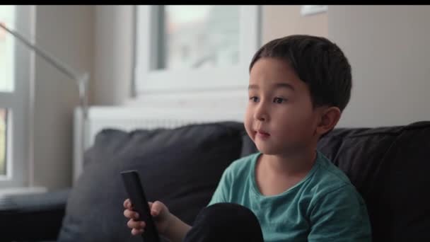 Kleiner süßer Junge schaltet Kanäle mit Fernbedienung am heimischen Fernseher — Stockvideo