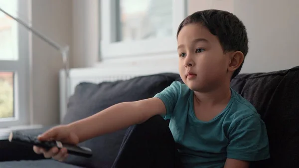 Malý roztomilý chlapec přepínač kanálů s dálkovým ovládáním v televizi doma — Stock fotografie