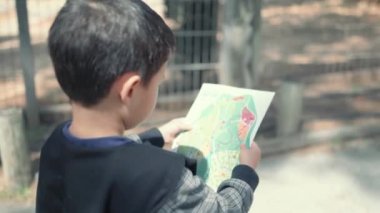 Küçük çocuk hayvanat bahçesinde harita çalışıyor.