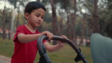 Cute child push baby stroller and walking in park. Siblings relationships and love.