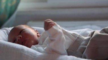 Newborn baby in white cries and calls parents to feed him. Baby moves his arms and legs