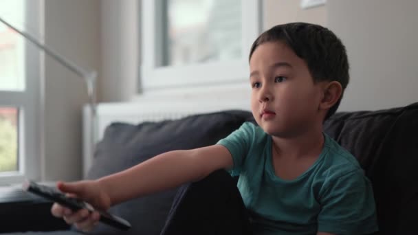 Evdeki TV 'de uzaktan kumandalı küçük şirin çocuk kanal değiştiriyor. — Stok video