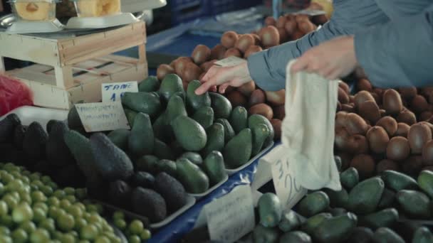 Vrouwelijke koper kiezen en zet avocado om milieuvriendelijke tas op de toonbank in de landbouwmarkt. Langzame beweging. Bewuste consumptie — Stockvideo