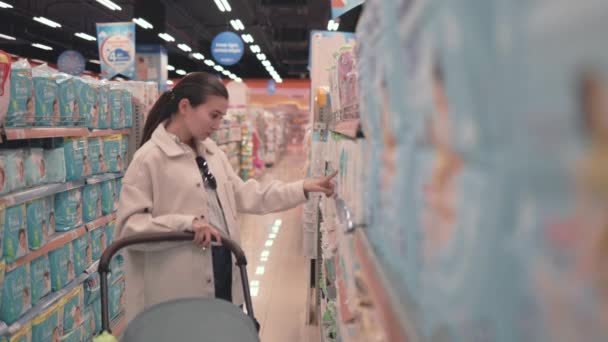 Asian woman in white choosing baby diapers in supermarket with stroller — Vídeos de Stock