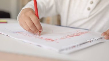 Beyaz kağıda kırmızı kalemle çizen küçük ellerin yakın plan görüntüsü.