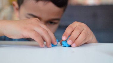 Little asian preschooler engaged in creativity. Boy plays with blue clay on the table