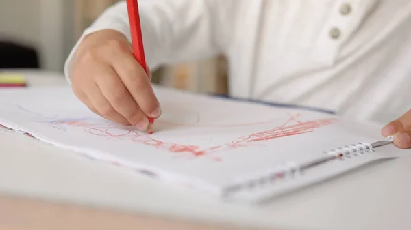 Vue rapprochée de petites mains dessinant avec un stylo rouge sur un papier blanc. — Photo