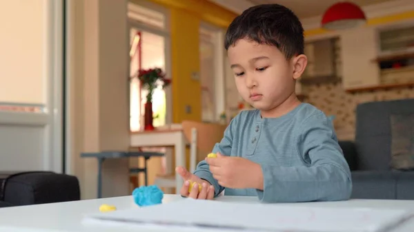 Little asian preschooler engaged in creativity. Boy takes a colourful clay and sculpts figures — ストック写真