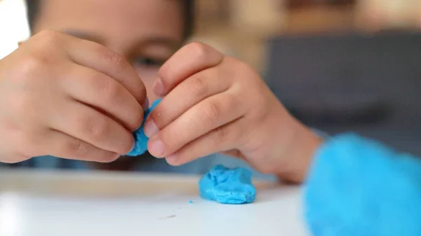 Little asian preschooler engaged in creativity. Boy plays with blue clay on the table — Zdjęcie stockowe