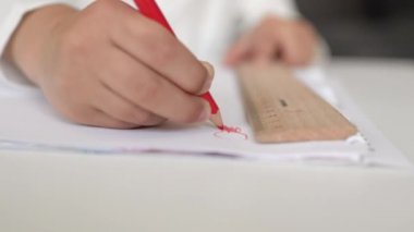 Beyaz kağıda kırmızı kalemle çizen küçük ellerin yakın plan görüntüsü.
