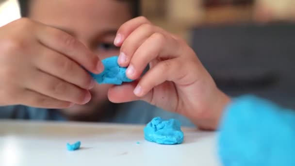 Malá asijská školačka se věnuje tvořivosti. Chlapec si hraje s modrou hlínou na stole — Stock video