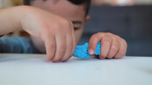 Kis ázsiai óvodás, aki kreativitással foglalkozik. A fiú kék agyaggal játszik az asztalon. — Stock videók