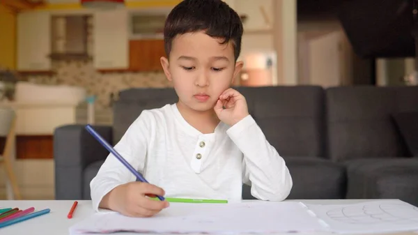 Kleiner asiatischer Junge in weißer Zeichnung mit blauem Stift auf Papier sitzt zu Hause — Stockfoto