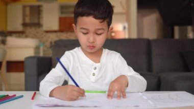 Beyaz çizim yapan küçük Asyalı çocuk. Elinde mavi kalemle evde oturuyor.