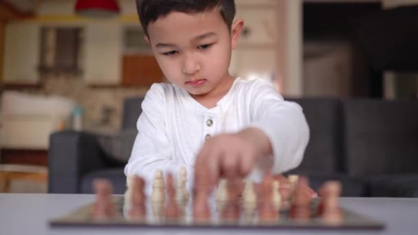 Front view of little boy in white playing chess on table — Stockvideo