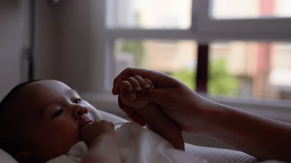 Bebê bonito em branco segurando as mães mão e chupa seu polegar — Fotografia de Stock