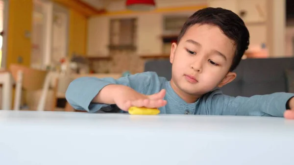 Mały azjatycki przedszkolak zaangażowany w kreatywność. Chłopiec tworzy kształt na stole — Zdjęcie stockowe