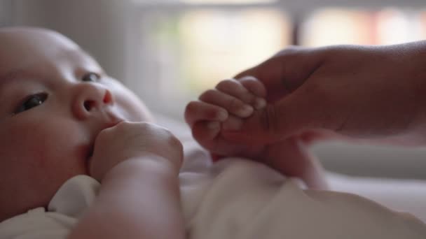 Cute baby in white holding mothers hand and sucks his thumb — Vídeos de Stock