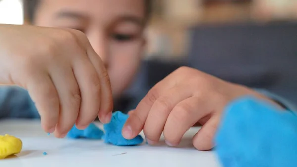 Widok z bliska na małego azjatyckiego przedszkolaka bawiącego się niebiesko-żółtą gliną na stole — Zdjęcie stockowe