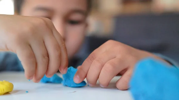 Close-up view of little asian preschooler playing with blue and yellow clay on the table — Zdjęcie stockowe