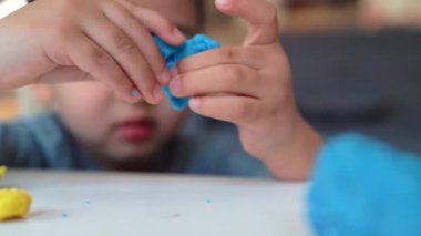 Masanın üzerinde mavi ve sarı kille oynayan bir çocuğun küçük ellerine yakından bakın.