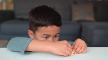 Küçük Asyalı anaokulu öğrencisi yaratıcılıkla meşgul. Çocuk masanın üzerinde bir figür yontuyor.