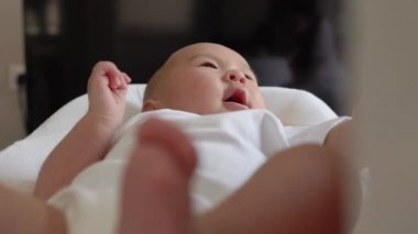 Beyazlar içindeki şirin bebek annesinin elini tutuyor ve onunla konuşuyor.